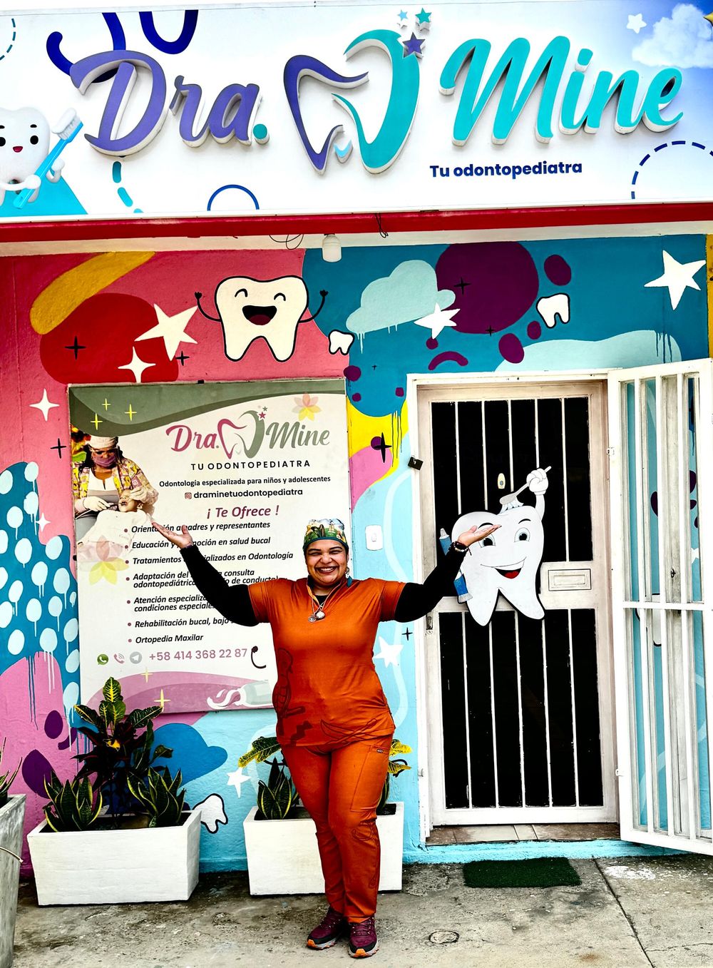 La Dra. Mine con los brazos abiertos frente a la fachada colorida del consultorio en Cabimas