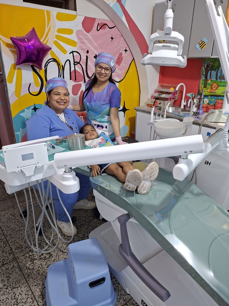 La Dra. Mine y su asistente junto a un niño recostado en el sillón odontológico, con el mural 