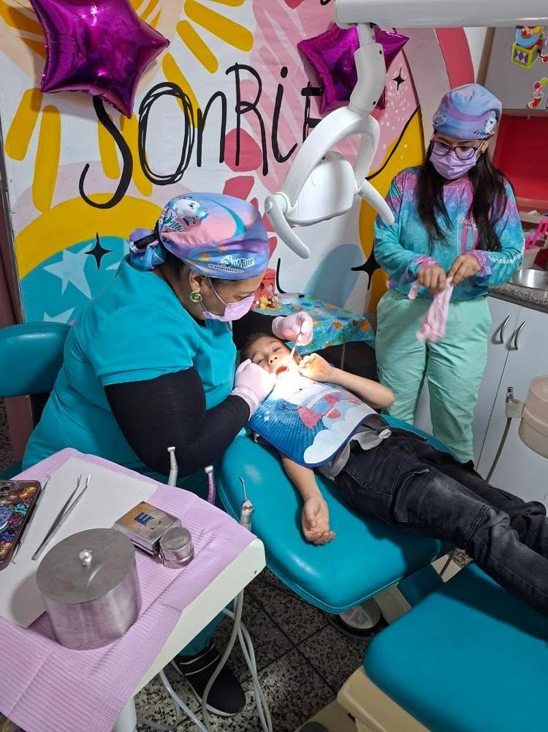 La Dra. Mine revisando la boca de un niño en el sillón mientras su asistente la apoya